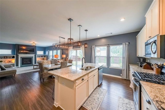 kitchen with appliances with stainless steel finishes, white cabinetry, an island with sink, sink, and light stone counters