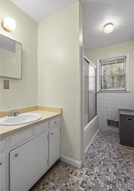 1729 Norden Rd, Riverdale, GA 30296 - bathroom with tile walls, a textured ceiling, visible vents, vanity, and shower / bath combination with glass door