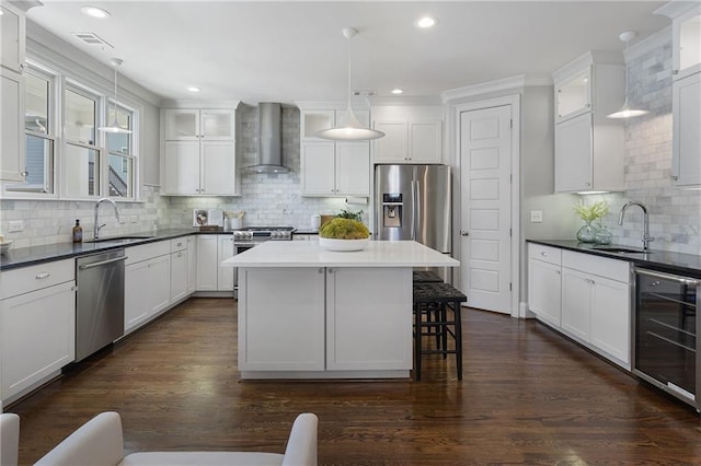 kitchen featuring appliances with stainless steel finishes, sink, beverage cooler, hanging light fixtures, and wall chimney range hood