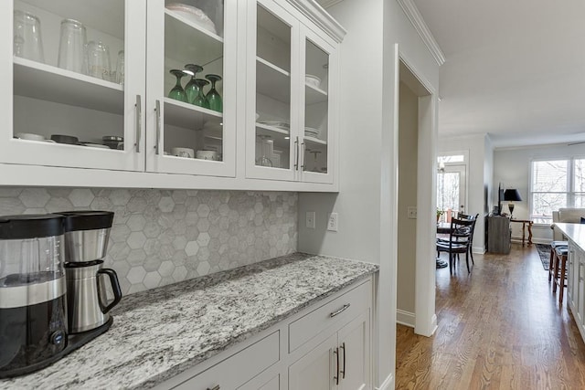 bar featuring light stone counters, tasteful backsplash, ornamental molding, dark hardwood / wood-style floors, and white cabinets