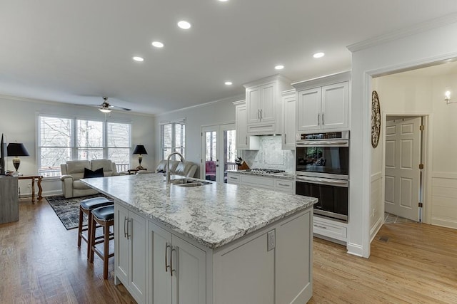 kitchen featuring white cabinetry, an island with sink, sink, light stone counters, and crown molding