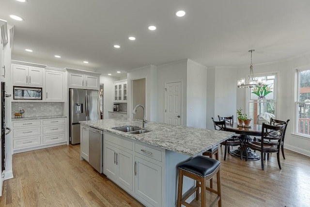 kitchen with appliances with stainless steel finishes, an island with sink, sink, white cabinets, and light hardwood / wood-style floors