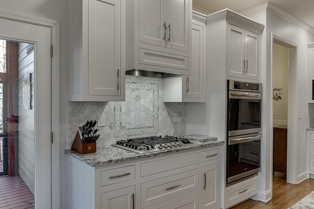 kitchen with stainless steel appliances, light stone countertops, white cabinets, and light hardwood / wood-style flooring