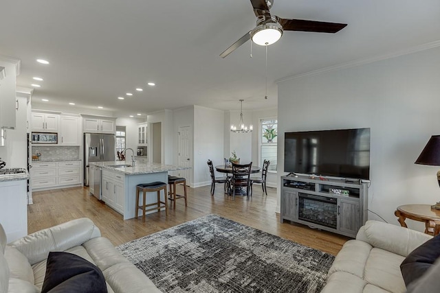 living room featuring crown molding, sink, ceiling fan with notable chandelier, and light wood-type flooring