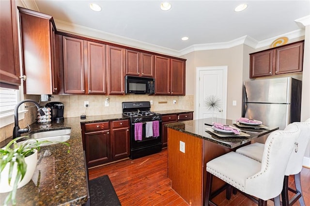 kitchen featuring dark wood-type flooring, sink, black appliances, dark stone countertops, and a kitchen island