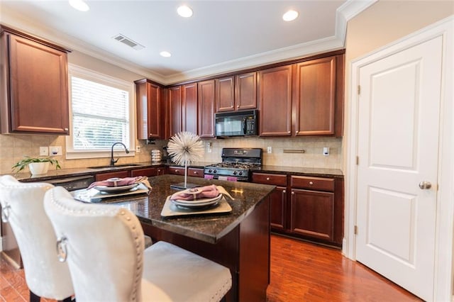 kitchen with sink, a center island, dark stone counters, a breakfast bar area, and black appliances