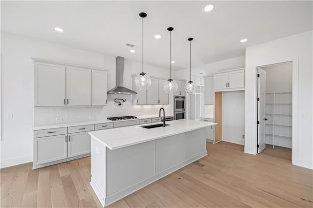 kitchen with pendant lighting, sink, white cabinetry, a center island with sink, and wall chimney exhaust hood