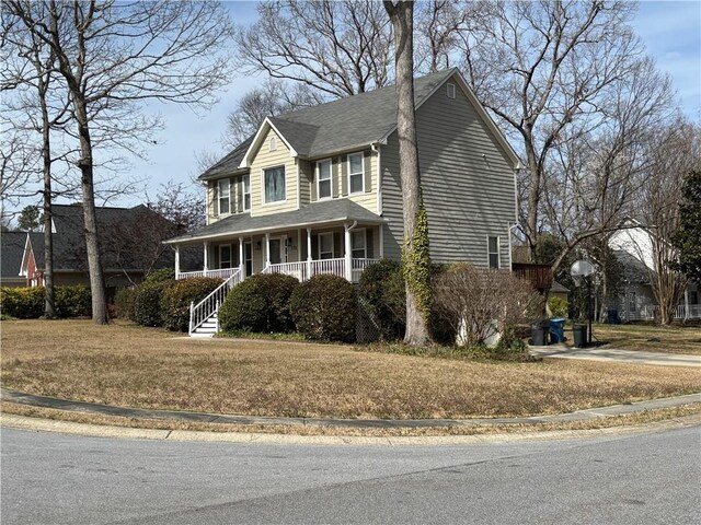 colonial inspired home with covered porch, a shingled roof, and a front yard