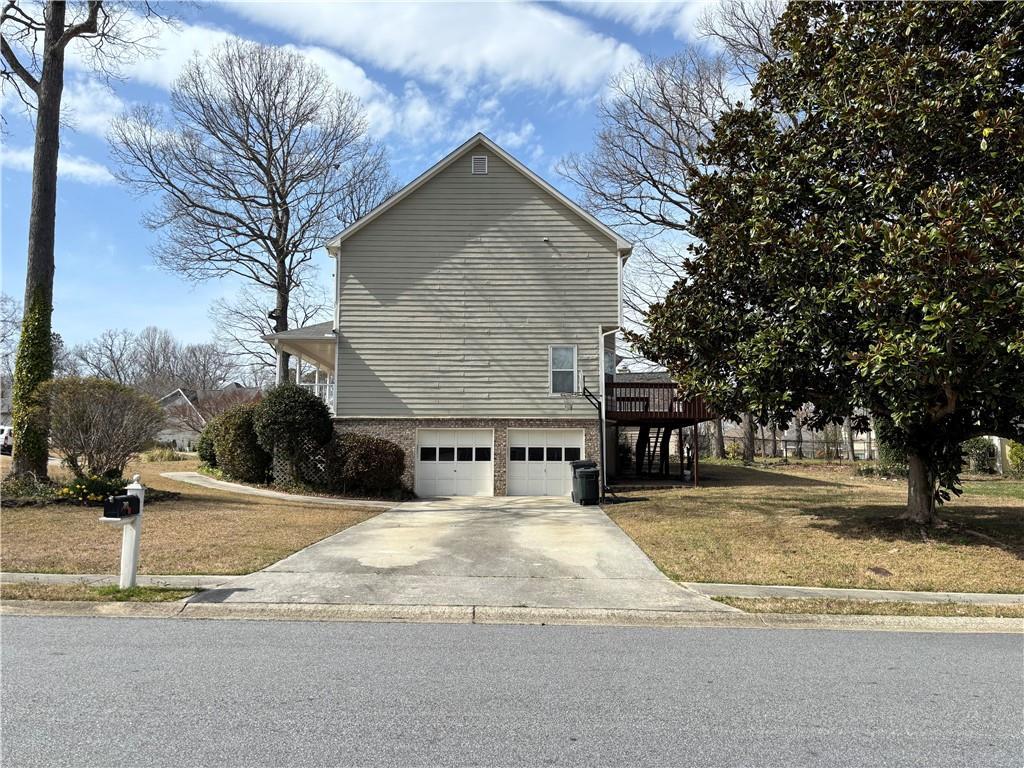 view of side of property featuring concrete driveway, central AC unit, a lawn, and an attached garage