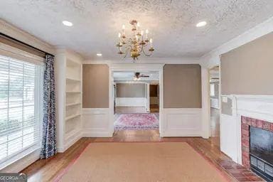 hall featuring an inviting chandelier, a textured ceiling, a wainscoted wall, recessed lighting, and wood finished floors