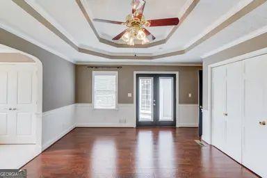 interior space with crown molding, wainscoting, wood finished floors, ceiling fan, and a raised ceiling