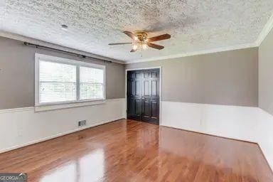 interior space featuring a textured ceiling, ceiling fan, ornamental molding, and wood finished floors