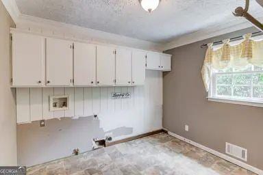 washroom with baseboards, laundry area, a textured ceiling, and visible vents