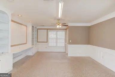 carpeted spare room with a ceiling fan, a wainscoted wall, and ornamental molding