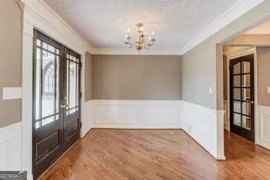 entrance foyer with ornamental molding, wainscoting, wood finished floors, french doors, and a notable chandelier