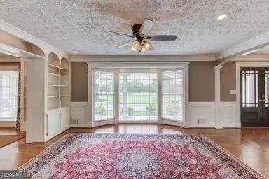 interior space with crown molding, ceiling fan, a decorative wall, a textured ceiling, and built in shelves