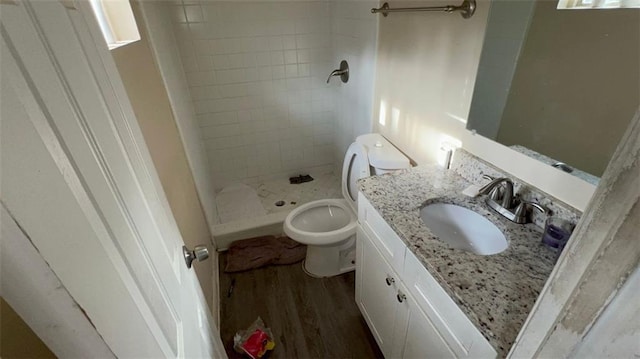 bathroom with toilet, vanity, wood-type flooring, and tiled shower