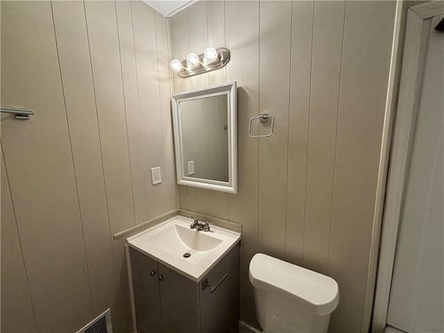 bathroom featuring wooden walls, vanity, and toilet