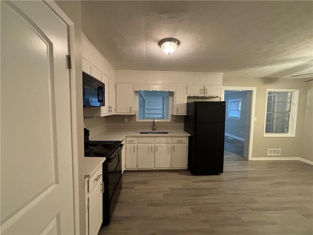 kitchen with a textured ceiling, sink, black appliances, hardwood / wood-style flooring, and white cabinetry