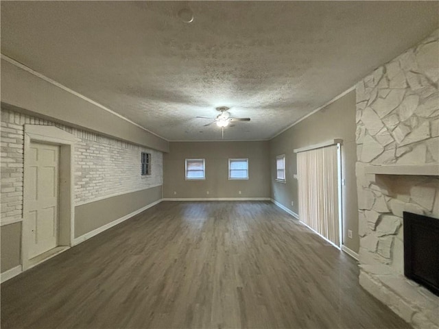 unfurnished living room with a textured ceiling, dark hardwood / wood-style floors, a stone fireplace, and crown molding