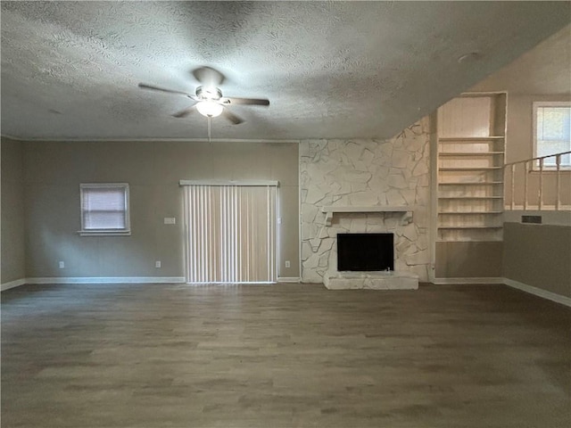 unfurnished living room featuring hardwood / wood-style flooring, ceiling fan, a stone fireplace, and a textured ceiling