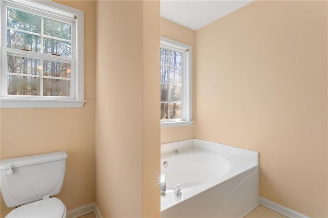 bathroom featuring toilet, a garden tub, and baseboards