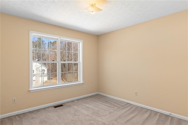 spare room featuring light carpet, baseboards, visible vents, and a textured ceiling