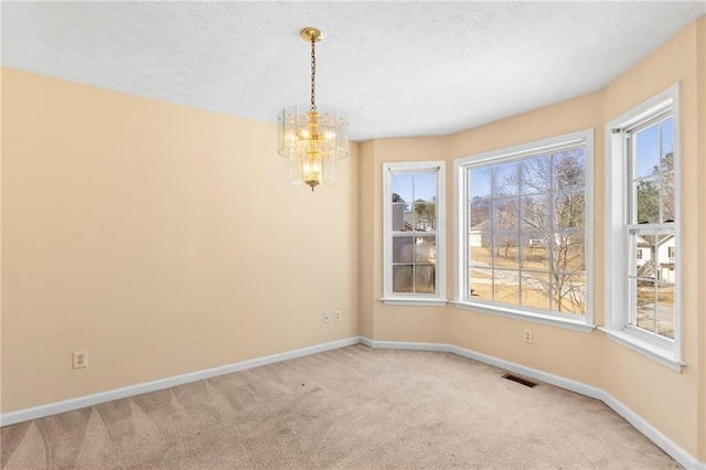 spare room with visible vents, baseboards, light colored carpet, an inviting chandelier, and a textured ceiling