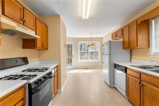 kitchen with under cabinet range hood, white dishwasher, brown cabinets, and range with gas stovetop