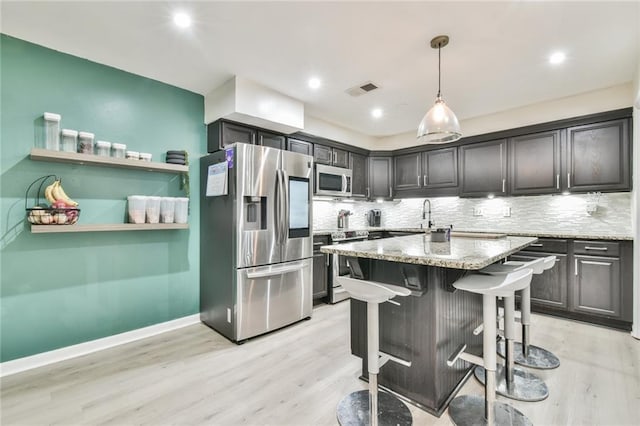 kitchen with pendant lighting, a breakfast bar area, light hardwood / wood-style flooring, appliances with stainless steel finishes, and light stone counters