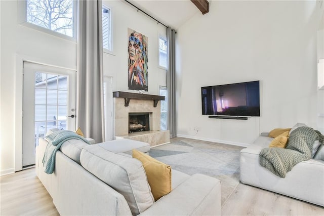 living room featuring beam ceiling, a wealth of natural light, light hardwood / wood-style floors, and a high ceiling