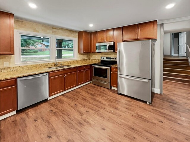 kitchen with light stone countertops, appliances with stainless steel finishes, light wood-type flooring, and sink