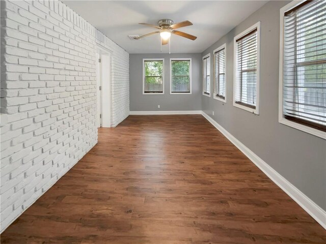 unfurnished room featuring brick wall, dark wood-type flooring, and ceiling fan