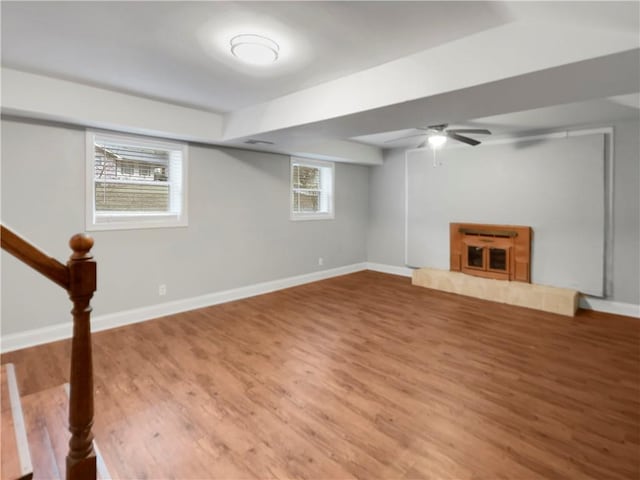 basement featuring a tiled fireplace, hardwood / wood-style flooring, plenty of natural light, and ceiling fan