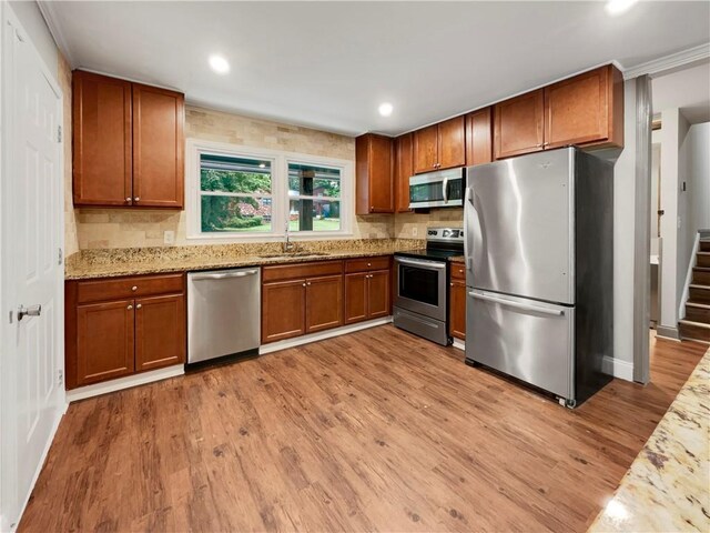 kitchen featuring light stone counters, sink, light hardwood / wood-style flooring, appliances with stainless steel finishes, and crown molding