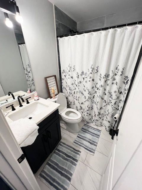 6060 Carriage Dr, Cumming, GA 30028 - full bath featuring vanity, toilet, marble look tile flooring, and curtained shower