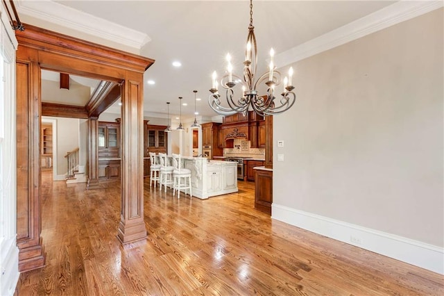 interior space featuring ornate columns, crown molding, light wood-type flooring, and an inviting chandelier