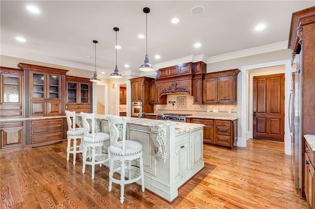 kitchen with light stone counters, a breakfast bar, pendant lighting, a center island with sink, and oven