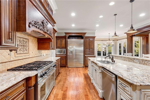 kitchen with light stone countertops, sink, pendant lighting, built in appliances, and a large island with sink