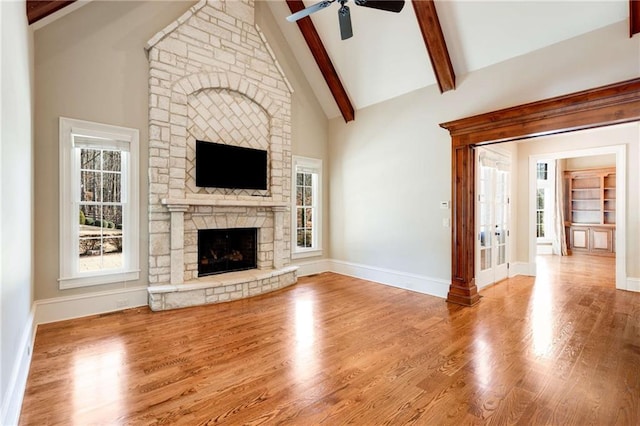 unfurnished living room featuring ceiling fan, beam ceiling, high vaulted ceiling, a fireplace, and light hardwood / wood-style floors