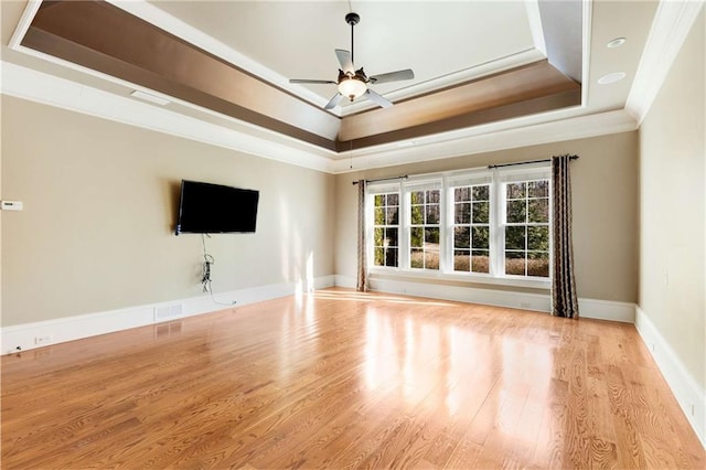 unfurnished living room with ceiling fan, a raised ceiling, ornamental molding, and light wood-type flooring