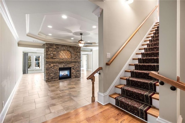 stairway with ceiling fan, a raised ceiling, crown molding, wood-type flooring, and a fireplace