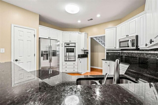 2709 Windrush Dr, Buford, GA 30518 - kitchen featuring appliances with stainless steel finishes, a warming drawer, white cabinetry, dark stone countertops, and a sink