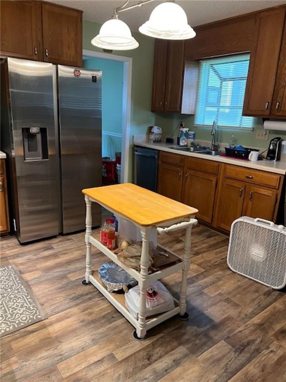 kitchen featuring black dishwasher, sink, decorative light fixtures, light wood-type flooring, and stainless steel refrigerator with ice dispenser