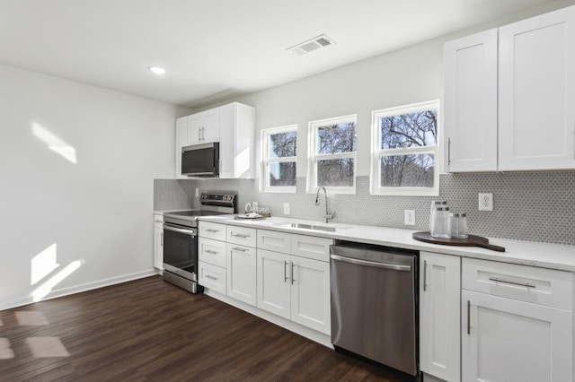 kitchen with stainless steel appliances, a sink, visible vents, light countertops, and tasteful backsplash