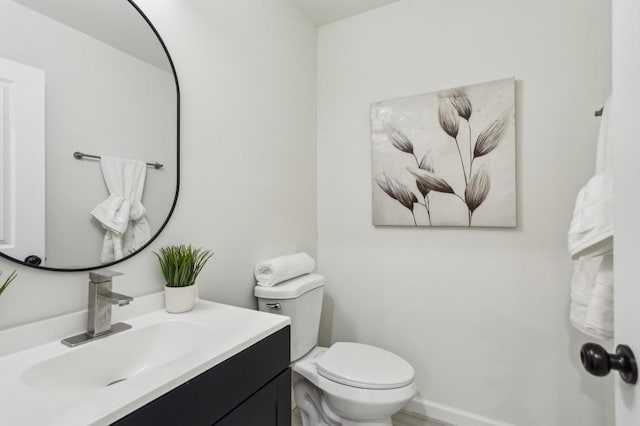 half bathroom with vanity, toilet, and baseboards