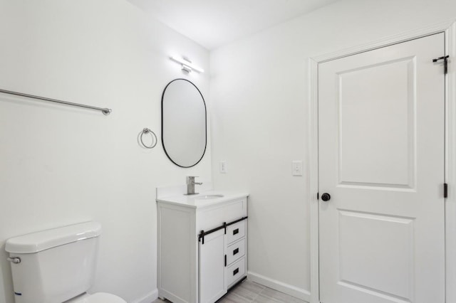 half bathroom featuring toilet, vanity, and baseboards