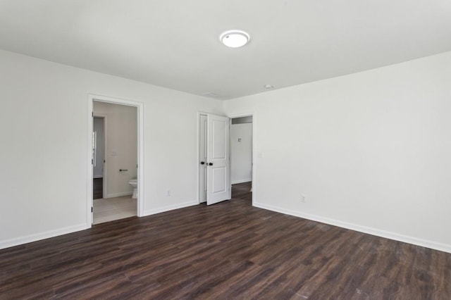 unfurnished bedroom featuring dark wood-style flooring, ensuite bath, and baseboards