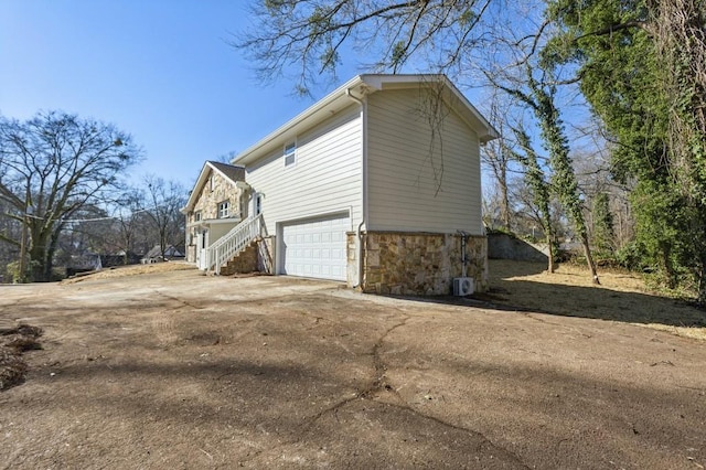 view of side of property featuring a garage, stone siding, and driveway