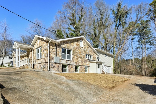 view of property exterior with a garage, stone siding, and driveway